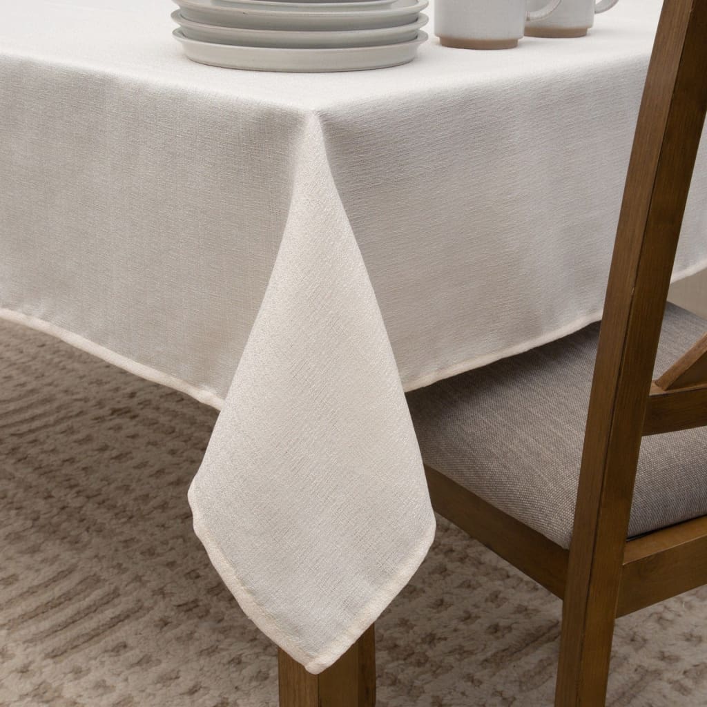 Beige linen tablecloth on a wooden dining table with chairs.